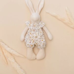 A soft, stuffed rabbit doll with a floral outfit and ruffled collar, placed on a beige background.