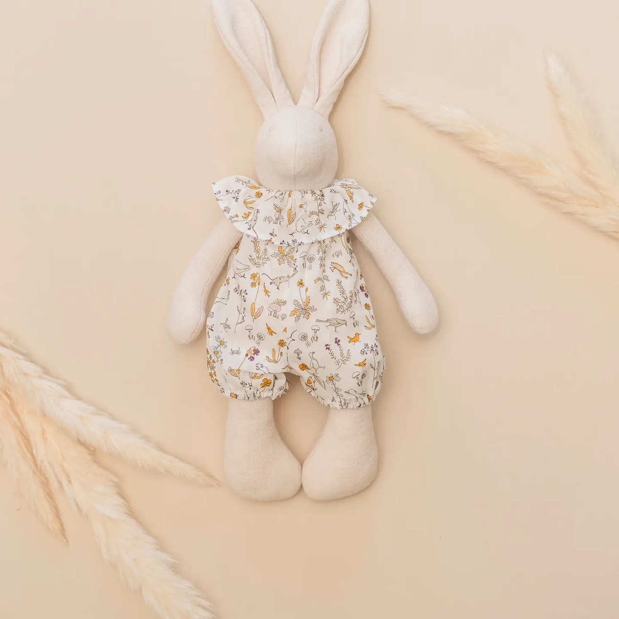 A soft, stuffed rabbit doll with a floral outfit and ruffled collar, placed on a beige background.