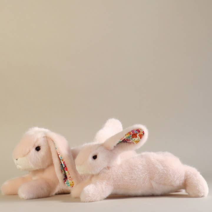 Two soft, plush rabbits lie side by side, featuring colorful patterned ears.