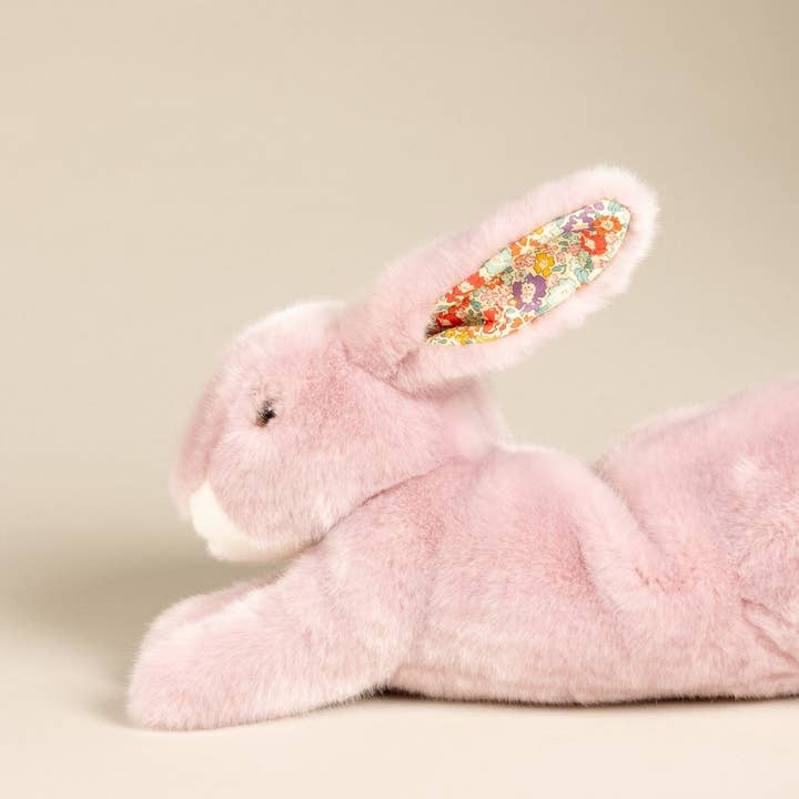 A soft pink stuffed rabbit with floral-patterned ears, lying on its side.