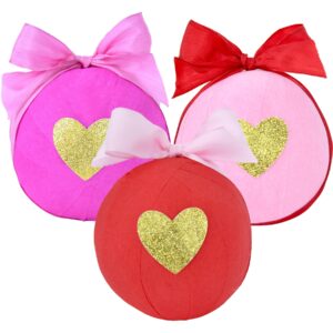 Three decorative surprise balls in pink, red, and light pink, each with a golden heart and ribbon bow.