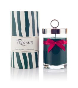 Scented candle in a glass jar with a silver lid and red ribbon, next to a decorative striped box.