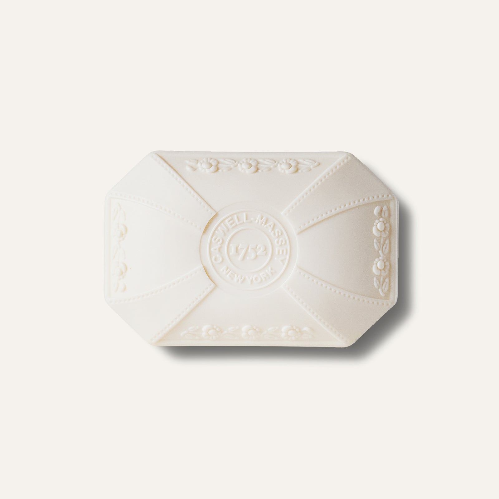 A rectangular bar of white soap with embossed floral designs and branding.