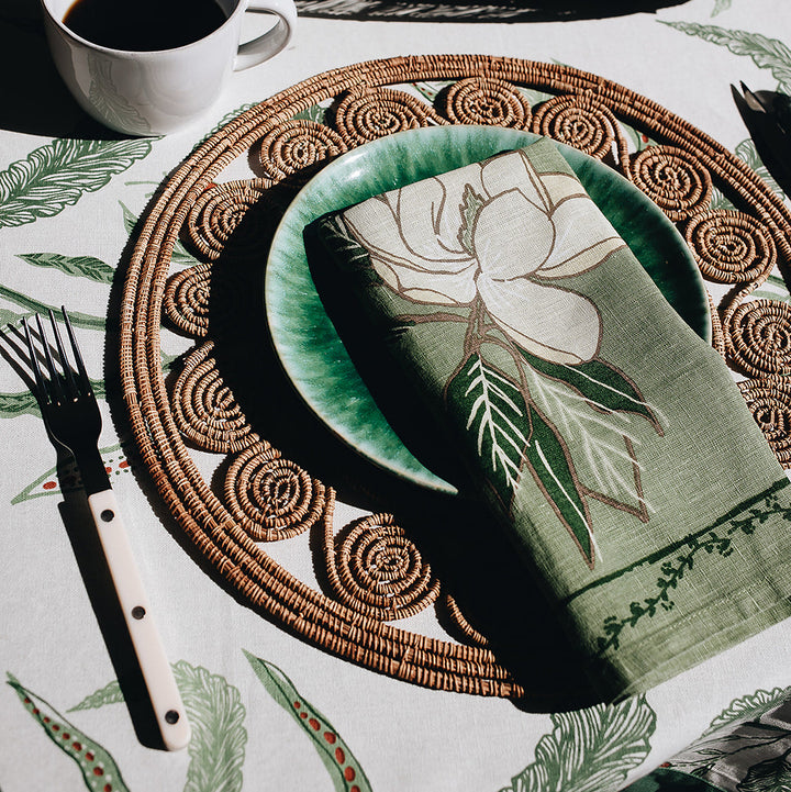 A green plate with a floral napkin sits on a woven placemat, alongside a fork and a cup of coffee.