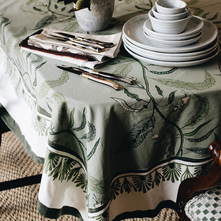 A table set with a patterned tablecloth, plates, cutlery, and a potted plant.