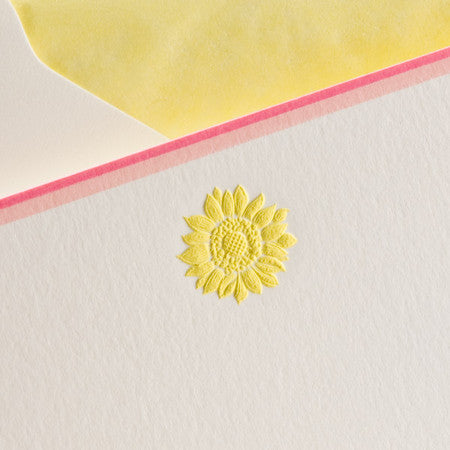 A yellow embossed sunflower on textured white paper with a pink border and a yellow background.