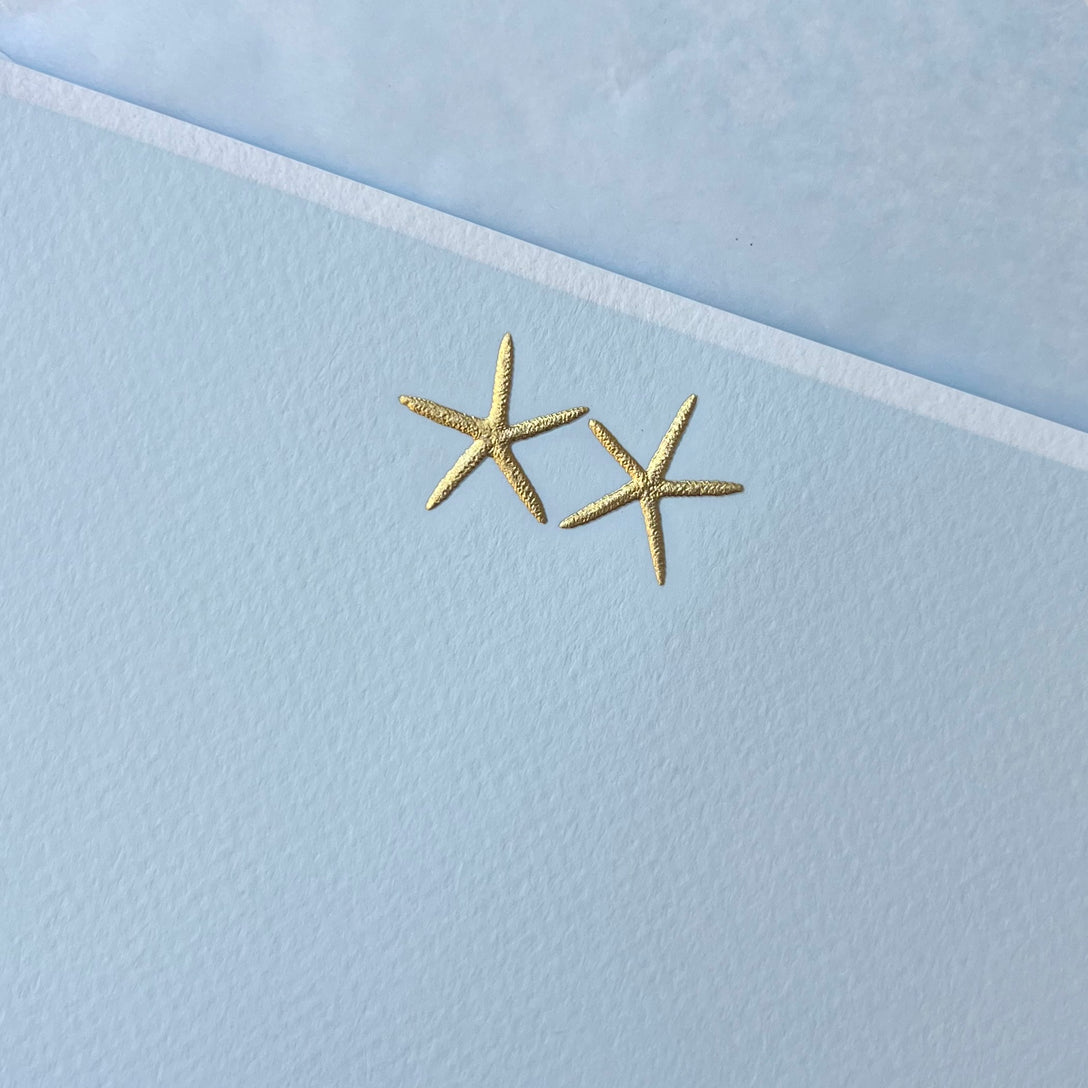 Two gold starfish on a light blue textured background.