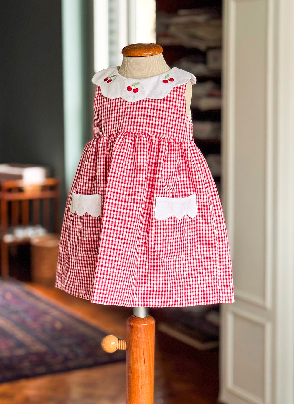 A red gingham dress with a white collar and cherry embroidery displayed on a mannequin.