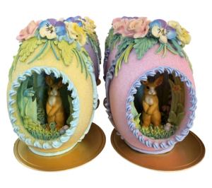 Two decorative sugar eggs with bunnies inside, adorned with flowers and greenery.
