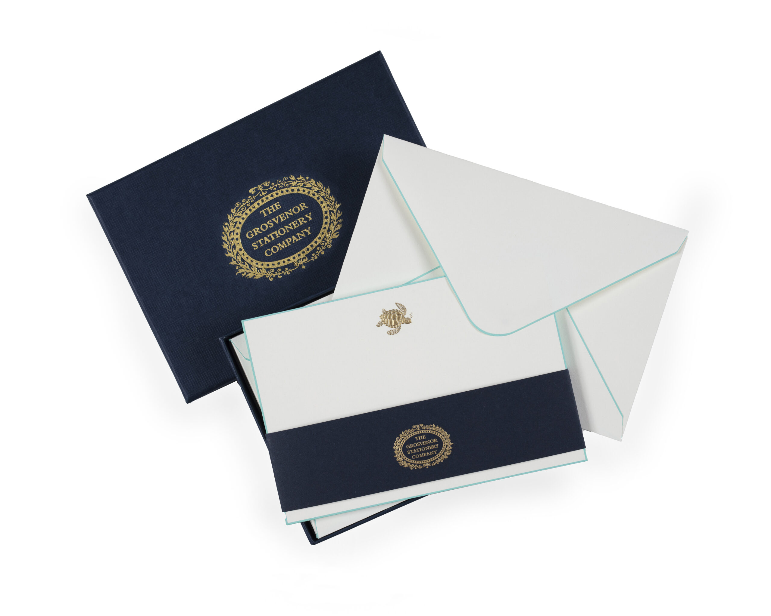 A navy stationery box contains white envelopes and cards, featuring gold and teal accents.