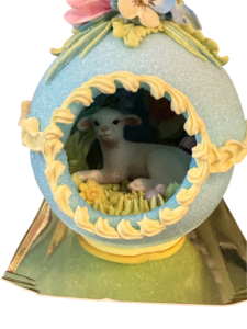 A decorative sugar egg featuring a lamb surrounded by flowers and grass inside.