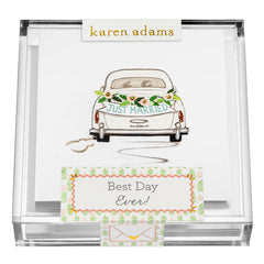 A decorated car with a "Just Married" sign and floral accents, alongside a card that says "Best Day Ever!