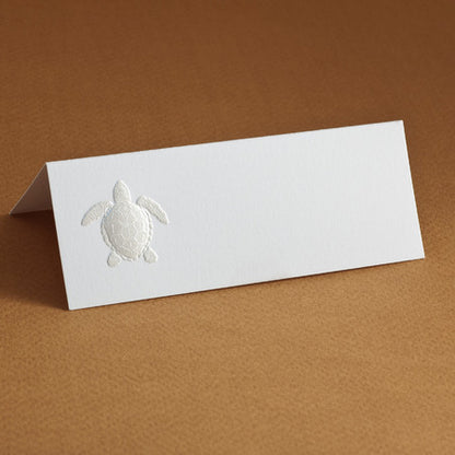 A white place card with an embossed turtle design on a brown surface.