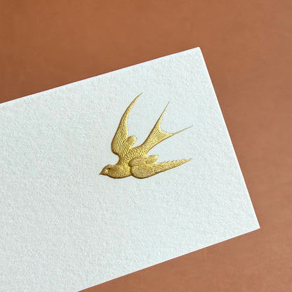 A white card features a gold embossed bird in flight against a brown background.