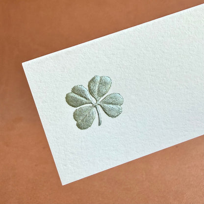 A textured white card features an embossed green four-leaf clover design.