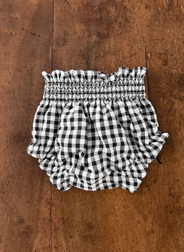 Black and white gingham baby bloomer shorts with ruffled edges on a wooden surface.