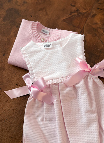 A pink sweater and a dress with pink ribbons lay on a wooden surface.