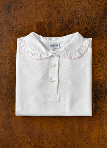 Folded white shirt with a ruffled collar and three buttons, resting on a wooden surface.