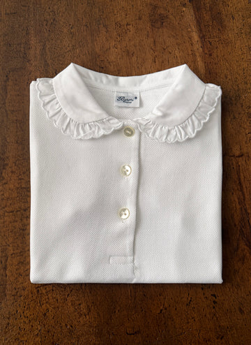 Folded white shirt with a ruffled collar and buttons, placed on a wooden surface.