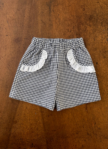 Black and white checkered shorts with ruffled pockets on a wooden surface.