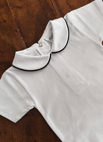White shirt with a black-trimmed collar, laid flat on a wooden surface.
