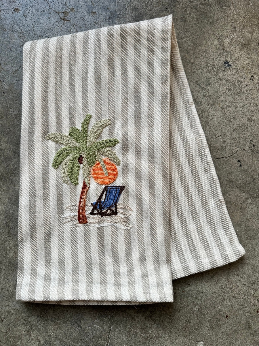 Striped towel featuring an embroidered palm tree, sun, and beach chair design.
