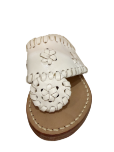 White sandal with decorative stitching and floral design on the strap, resting on a light brown sole.